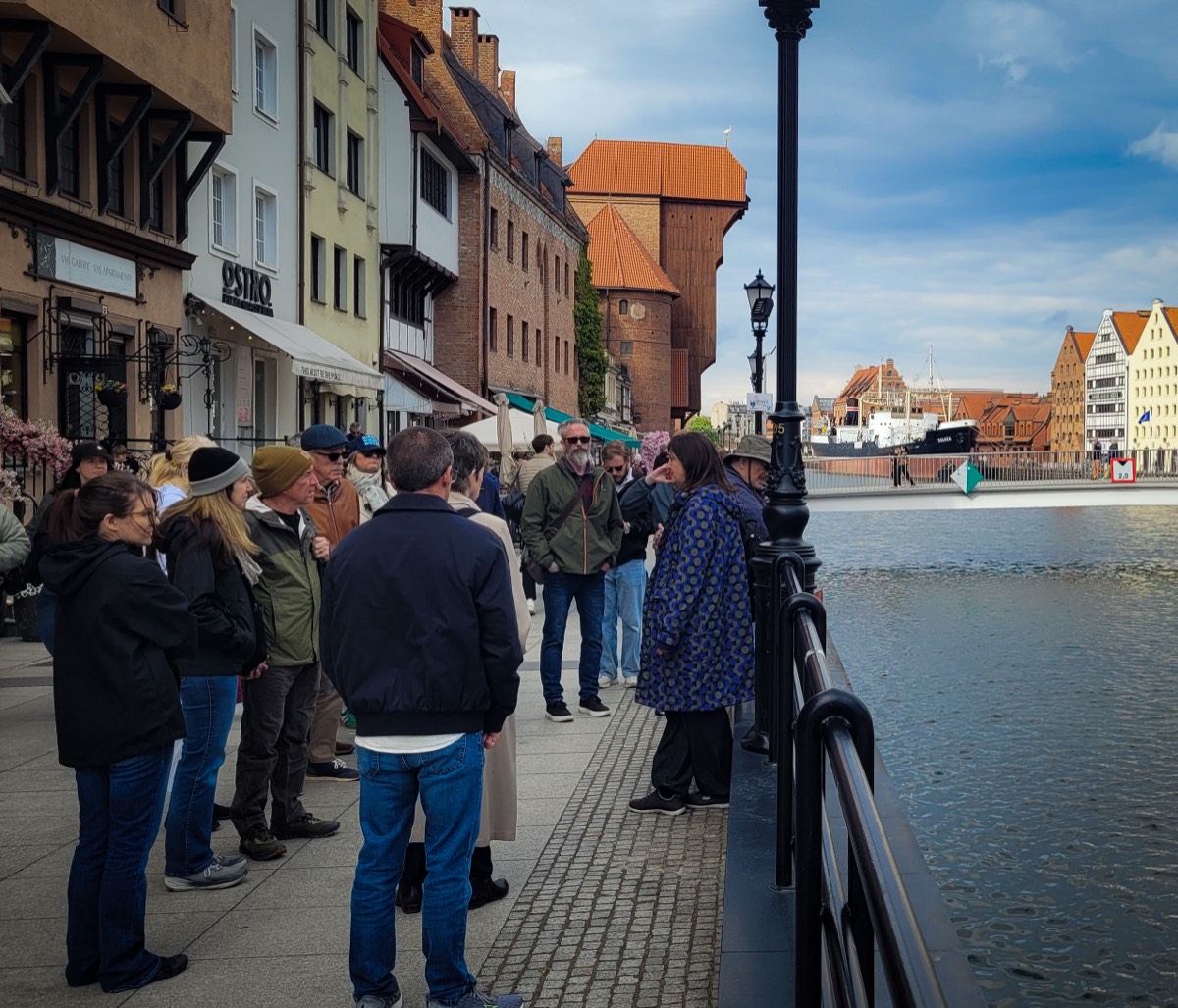 A guide talking to a group on the Motława waterfront in Gdańsk, with the medieval Crane and historic granaries across the water